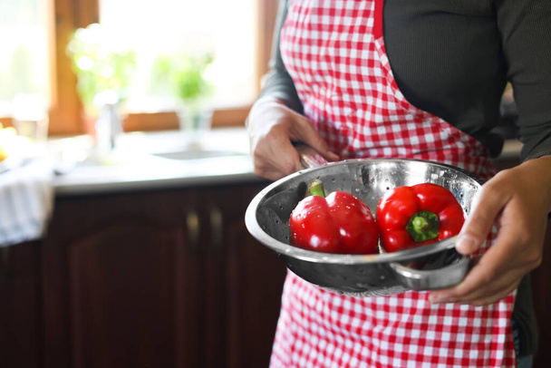 Woman holding colander with fresh bell peppers in kitchen, closeup. Space for text - Фото, зображення