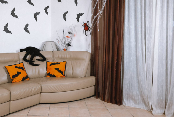 Interior of the living room decorated for Halloween with orange paper spider or bats on the wall.Modern interior of the home room decorated for Halloween sofa with orange pillows. - Foto, Imagem