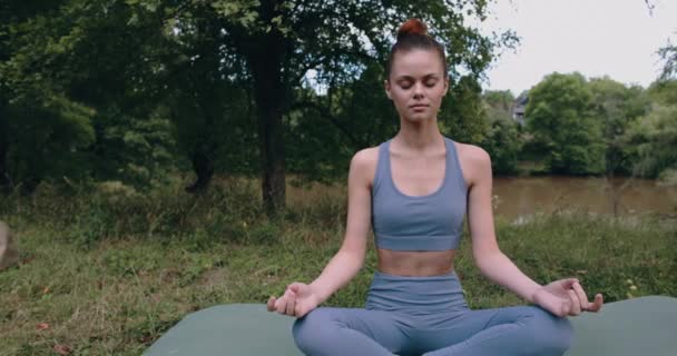 Женщина медитирует в позе лотоса, выполняя низкую йогу асану на открытом воздухе в парке в спортивной одежде на зеленой траве летом. Высококачественные 4k кадры - Кадры, видео