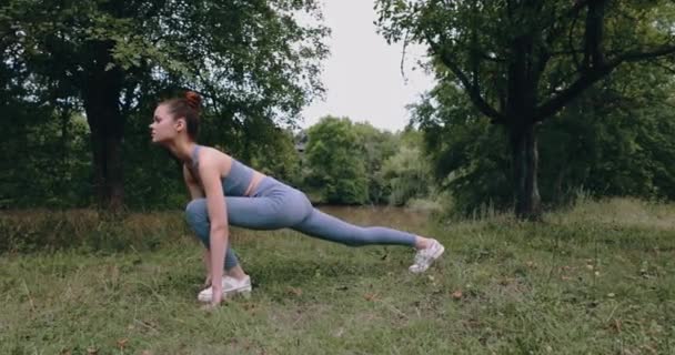 Jonge vrouw doet fitness stretching voor gymnastiek buiten in het park buiten staan op groen gras, levensstijl. Hoge kwaliteit 4k beeldmateriaal - Video