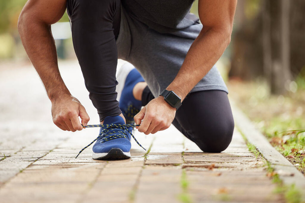 You better get ready for some big results. Closeup shot of an unrecognisable man tying his shoelaces while exercising outdoors - Foto, immagini