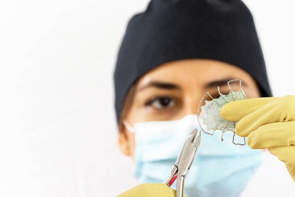 young female dentist holding dental instruments in her hand, protected by a glove on a white background and wearing a mouth cover. - Foto, Imagen