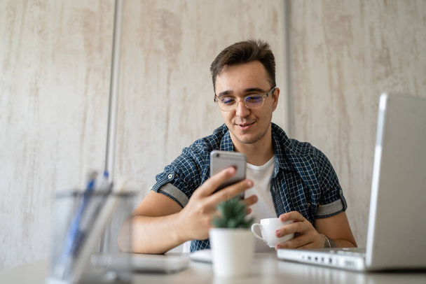 Yksi mies valkoihoinen mies istuu tuolissa toimistossa töissä työpöydällä matkapuhelimella soittaakseen työskennellessään projektin kulumista sininen paita ja silmälasit puhuvat onnellinen hymy kopioi tilaa - Valokuva, kuva