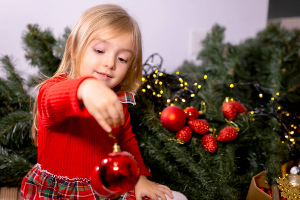 Young girl helping her mother decorating the Christmas tree, holding some Christmas baubles in her hand. High quality photo - Foto, Bild