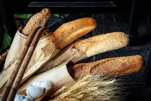 Freshly baked bread lies in a wicker basket. Several different fresh loaves in eco-package along with ears of wheat. - Foto, immagini
