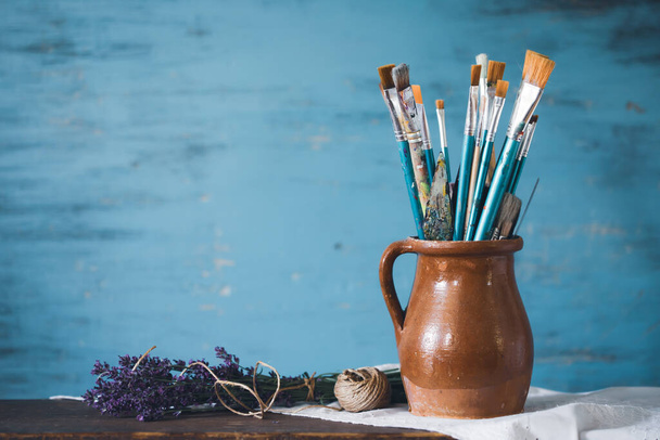 Still life of paint brushes  in clay jug an lavender flower on vintage turquoise background - Foto, Bild