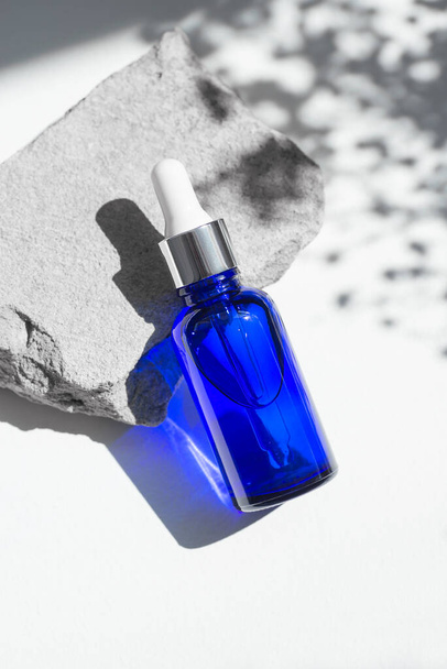Blue dropper bottles with serum, tonic or essential oil on grey concrete podium. White background with daylight with flowers shadows. Beauty concept for face and body care - Foto, Imagem
