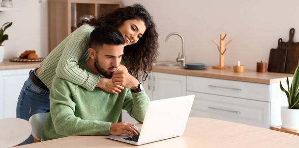 pareja joven utilizando el ordenador portátil en la cocina - Foto, imagen