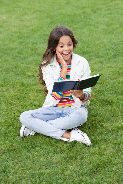 surprised teen girl read book sitting on grass. reading book. reader girl with book outdoor. - Photo, image