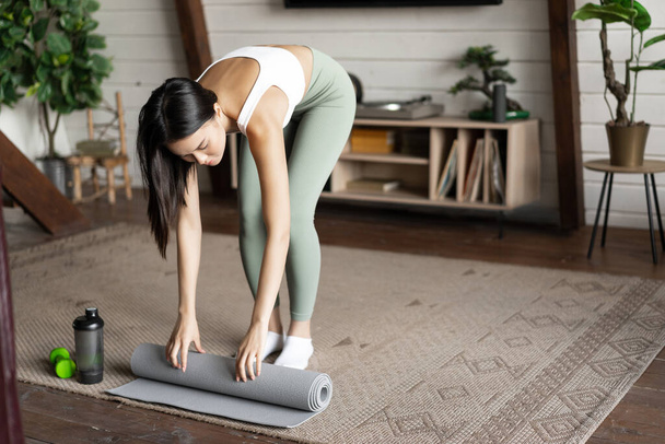 Ázsiai fitness lány befejezni edzés, edzés otthon, gördülő padló szőnyeg után gyakorlatok a nappaliban. - Fotó, kép