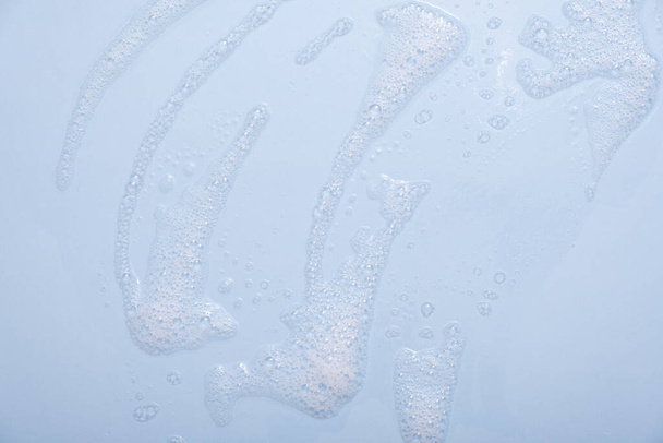 Muestra de mousse limpiador facial. Burbujas blancas de espuma limpiadora sobre fondo azul. Jabón, gel de ducha, champú textura de espuma de primer plano. - Foto, imagen