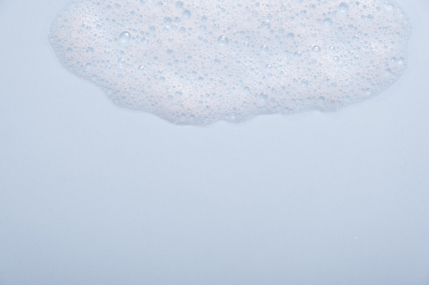 Muestra de mousse limpiador facial. Burbujas blancas de espuma limpiadora sobre fondo azul. Jabón, gel de ducha, champú textura de espuma de primer plano. - Foto, imagen