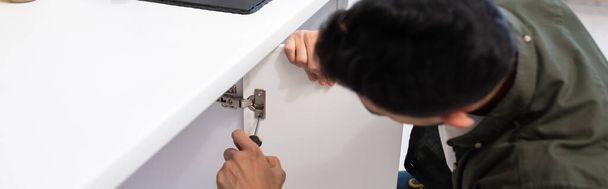Blurred man with screwdriver fixing door of cabinet in kitchen, banner  - Foto, Imagen