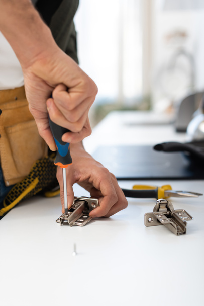 Cropped view of man with screwdriver fixing hinge of cupboard  - Foto, immagini