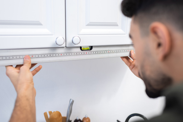 Blurred muslim craftsman measuring level of kitchen cabinet at home  - 写真・画像