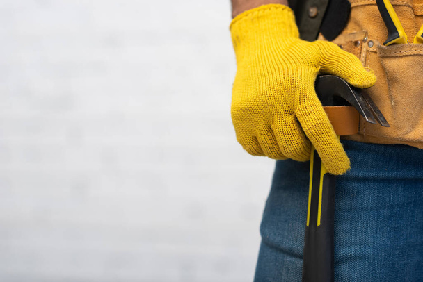 Cropped view of craftsman in glove holding hammer in tool belt at home  - Zdjęcie, obraz