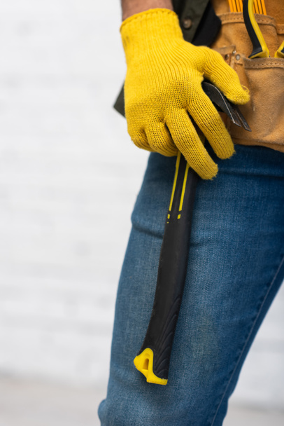 Cropped view of repairman in glove holding hammer on tool belt at home  - Photo, Image