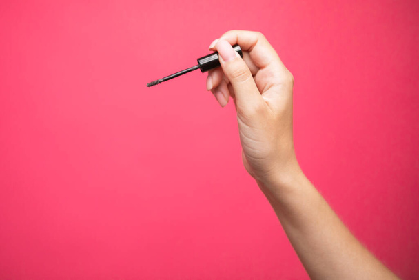 Close up of womans hand holding an eyebrows brush mascara on pink background. High quality photo - 写真・画像