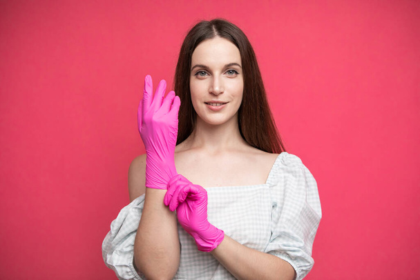 Young woman puts on protective surgical sterile gloves on her arm, isolated on pink background. High quality photo - 写真・画像