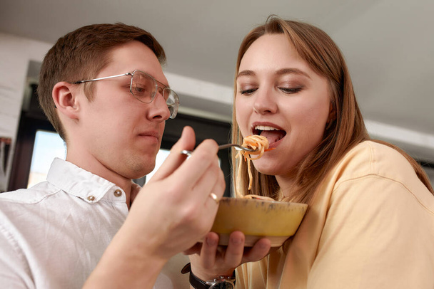 Smiling loving husband feeding wife, young couple enjoying tender moment, romantic date, having fun, eating japanese cuisine, happy family spending free weekend in modern kitchen. - Zdjęcie, obraz