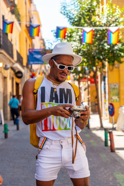 Portrait of a gay black ethnicity man at the pride party looking at the photos on the camera, LGBT flag - Foto, Bild