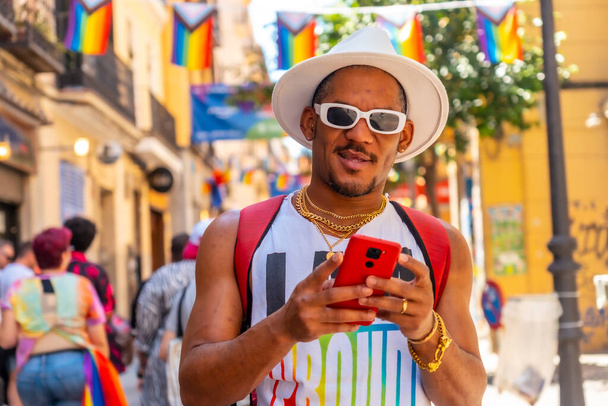 A gay black man at the pride party writing a message with the phone, LGBT flag - Фото, зображення