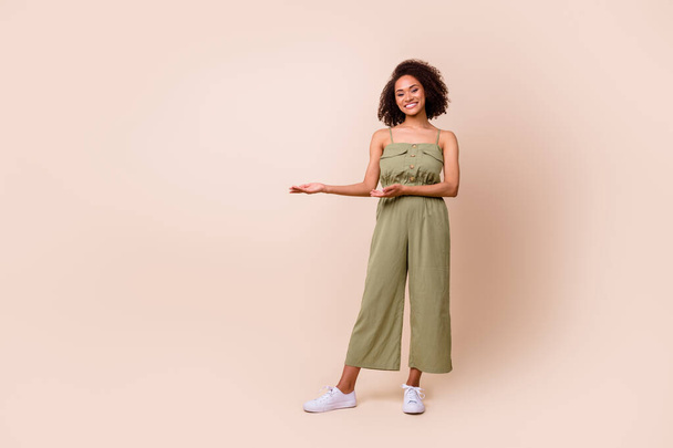 Full size photo of adorable pretty cheerful woman wavy hairdo khaki overall demonstrating empty space isolated on beige color background. - Φωτογραφία, εικόνα