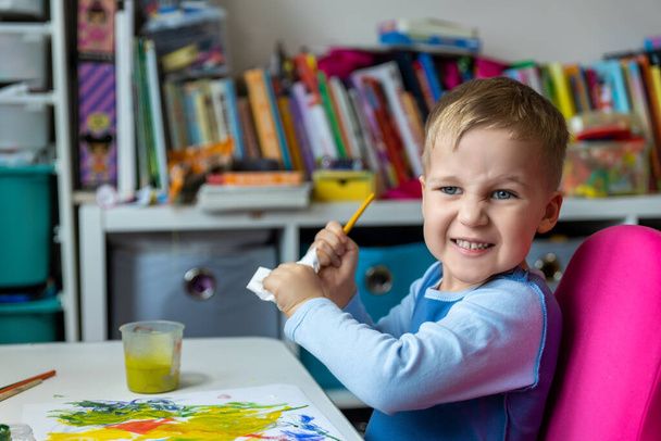 Portrait of cute little blond kid boy enjoy have fun painting with watercolor and brush bright abstract inage on paper at home or kindergarten class. Imagination development children play activity. - Photo, Image
