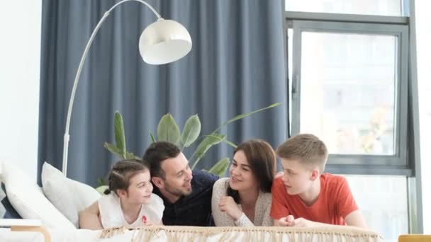 Mom, dad and two children are lying on the sofa in the living room with a modern interior and talking happily. Family vacation - Filmagem, Vídeo