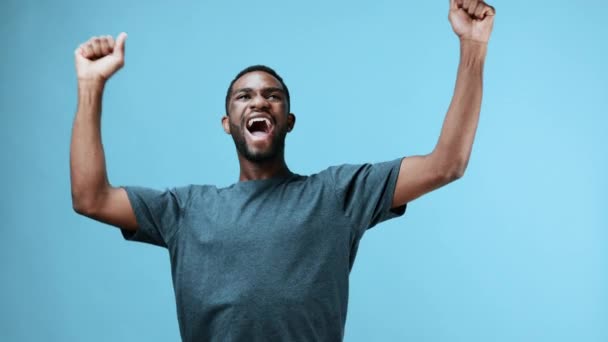Felice uomo afroamericano è felice e si rallegra della vittoria alzando le mani con pugni serrati. Filmati 4k di alta qualità - Filmati, video