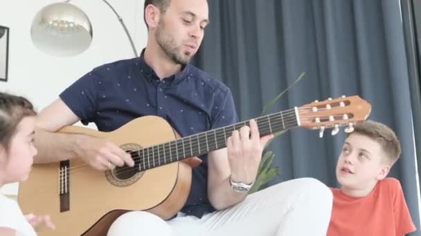 Cheerful man playing guitar and singing with children. Happy family weekend at home. - Video