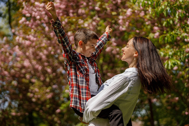 Portrait of beautiful young mother with little cute son on hands in summer park with trees blossom. - Foto, Bild