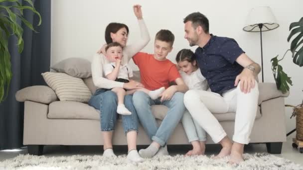 A happy husband and wife with three children are sitting on a bright sofa in the living room and hugging. Great family time together. Family photo session - Séquence, vidéo