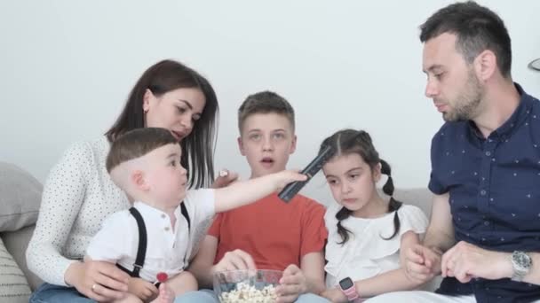 A large family with three children spends the weekend at home in front of the TV and eating popcorn. Family time together - Materiał filmowy, wideo