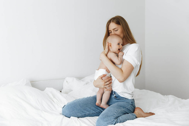 young caring mother hugged her little daughter, pressing her to her chest. Beautiful woman holding a newborn baby in her arms at home. Smiling mother hugging a small newborn baby showing love and care. motherhood concept, mother's day - Фото, зображення