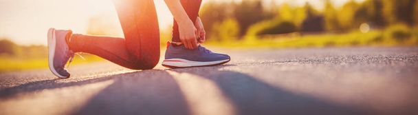 Sporty woman tying shoe laces before starting to run. Sunset in nature. Concept of healthy lifestyle. - Фото, изображение