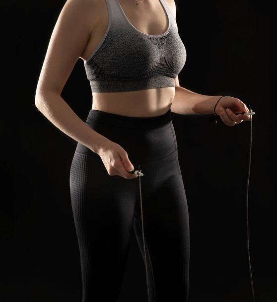 Close up picture of athletic woman performing exercise with jumping rope on the black background - Fotoğraf, Görsel