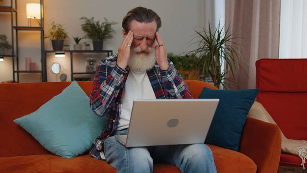 Втомлений старший дід фрілансер використовує ноутбук, страждаючи від головного болю проблеми напруги та мігрені, стресу. Літній чоловік працює на ноутбуці, надсилає повідомлення, здійснює онлайн-покупки, переглядає фільми
 - Фото, зображення