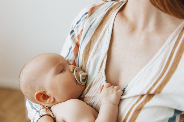 Loving mother takes care of her newborn baby at home. Portrait of a happy mother holding a sleeping baby in her arms. The mother hugged her little baby. Love of mother and child. family at home, education, breastfeeding - Foto, Bild