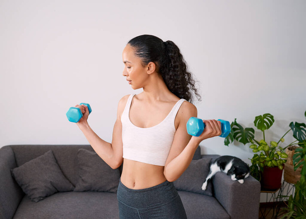 A serious young woman lifts weights to get strong at home. High quality photo - Zdjęcie, obraz