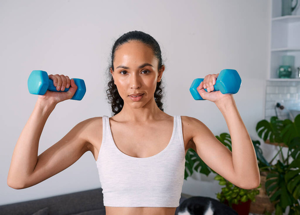 A serious young woman lifts weights to get strong at home. High quality photo - 写真・画像