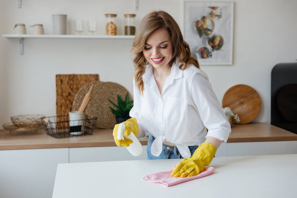 Housewife in yellow gloves wipes the kitchen table. High quality photo - Foto, afbeelding