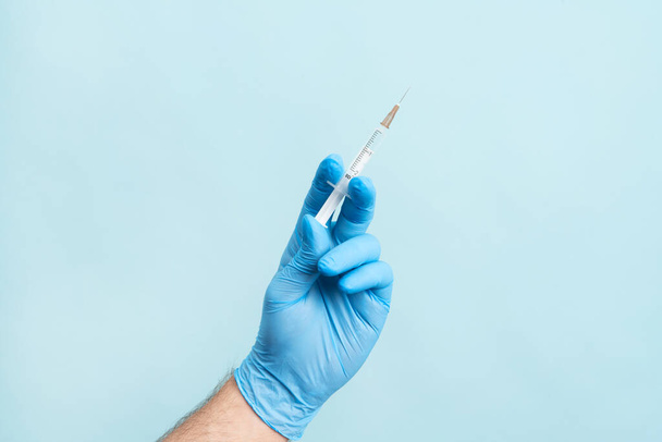 Close up picture of male hand with nitrile glove holding a syringe with vaccination on the blue background. Health care, vaccination cocncept. - Фото, изображение