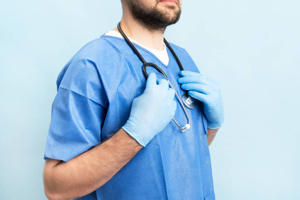 Portrait of smilin young and motivated doctor with stethoskope over neck and medical scrubs standing on the blue background. - Foto, Bild