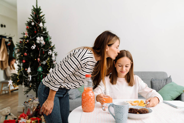 White mother kissing her daughter while having breakfast at home - 写真・画像
