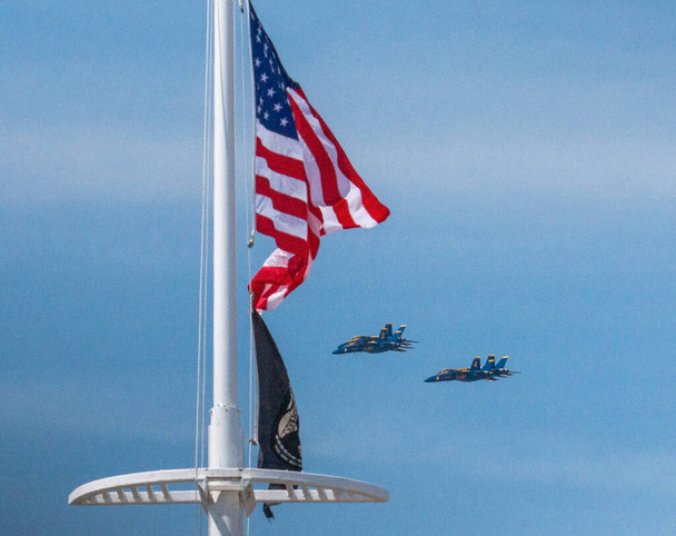 U.S. Navy Blue Angels flying in formation behind an American Flag blowing in the wind during an airshow. - Photo, image