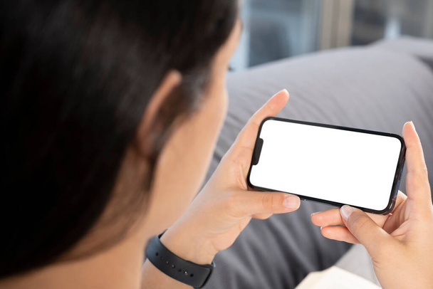 Smartphone mock up, close up over shoulder view of woman holding smartphone mock up. Young caucasian female looking white blank screen, watching video, online education or meeting concept idea photo. - Photo, Image