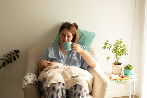 La mujer bebe té o café durante el proceso de amamantar al bebé recién nacido. Lactancia materna cómoda - Foto, imagen