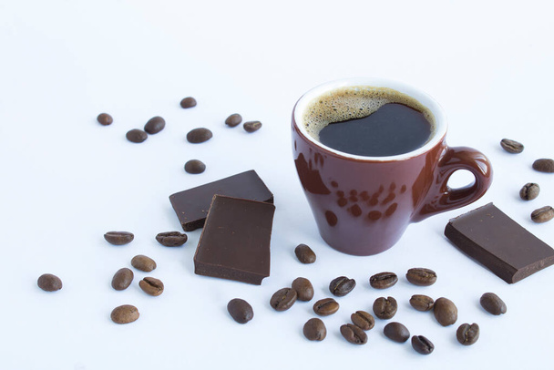 Black coffee in the brown cup, coffee beans and pieces of chocolate on the white  background. Closeup. - Φωτογραφία, εικόνα