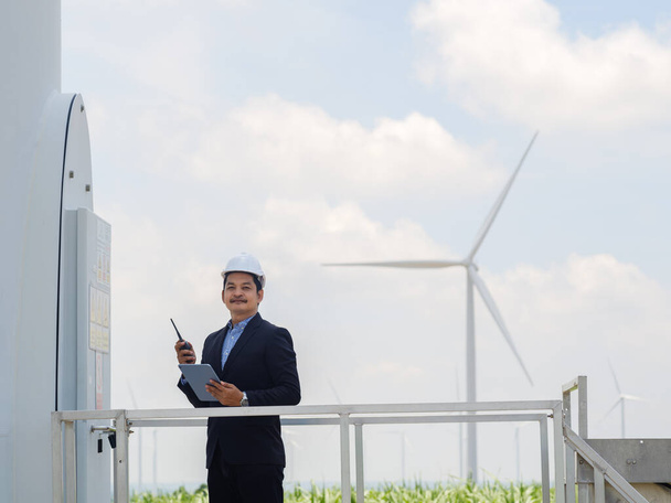 Asian engineer manager in a suit is using a tablet to control and monitor the operation of a wind turbine in the electrical control room.Concept of sustainability development by alternative energy - Φωτογραφία, εικόνα